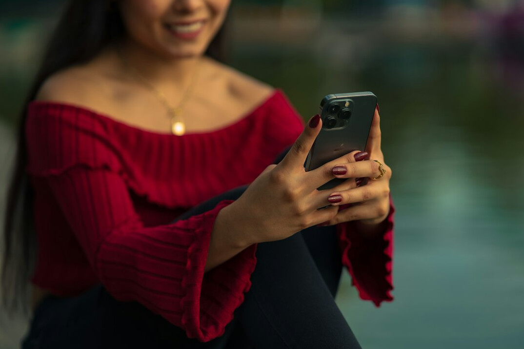 Joven latina sonriente sosteniendo un teléfono móvil para redes sociales